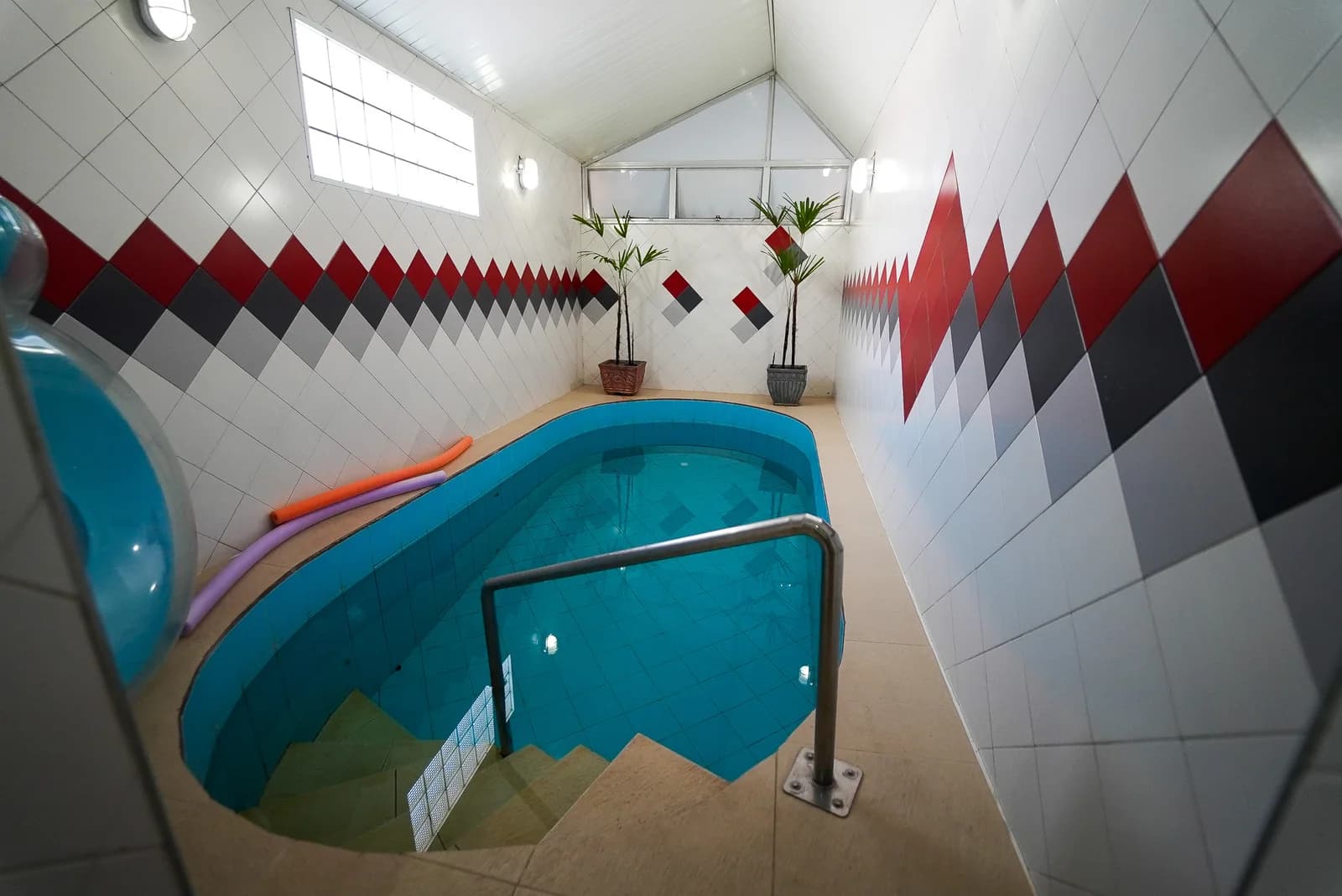Piscina interna com degraus, corrimão e revestimento geométrico