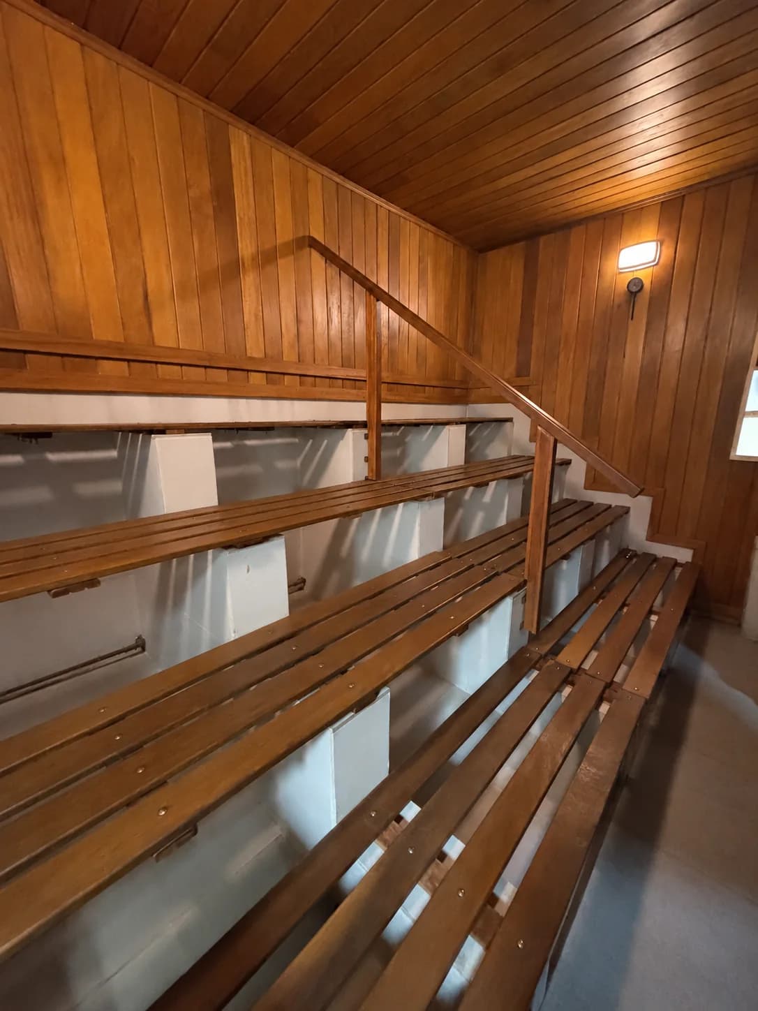 Sauna seca reformada com bancos de madeira em níveis e corrimão